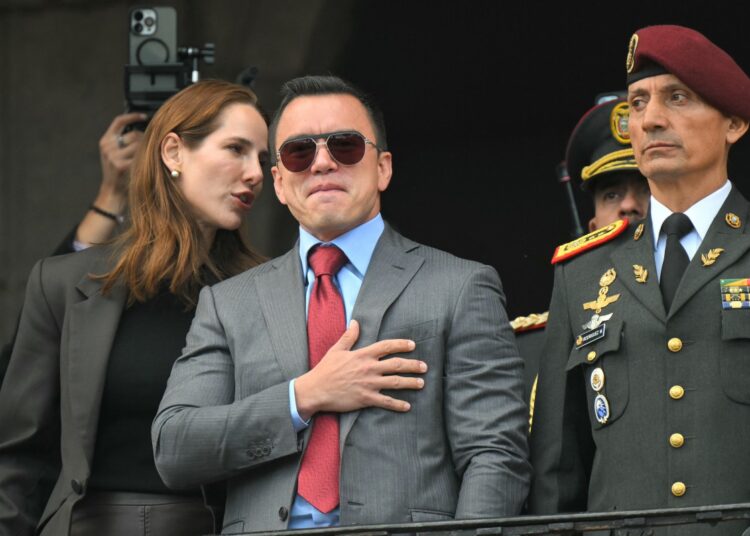 Ecuador's President reelect Daniel Noboa (C) acknowledges supporters accompanied by his wife, Lavinia Valbonesi (L) and the chief of the Presidential Military House, Milton Rodriguez, from a balcony of the Carondelet Presidential Palace during the changing of the guard ceremony in Quito on April 15, 2025. Ecuador's President reelect Daniel Noboa faces the herculean task of uniting his violence-struck nation, after his leftist rival Luisa Gonzalez called his victory into question. (Photo by Rodrigo BUENDIA / AFP)